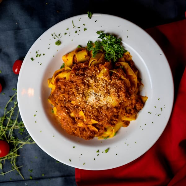 La Bella Luna's pappardelle pasta with rich bolognese sauce, parmesan, and fresh parsley on a white plate.