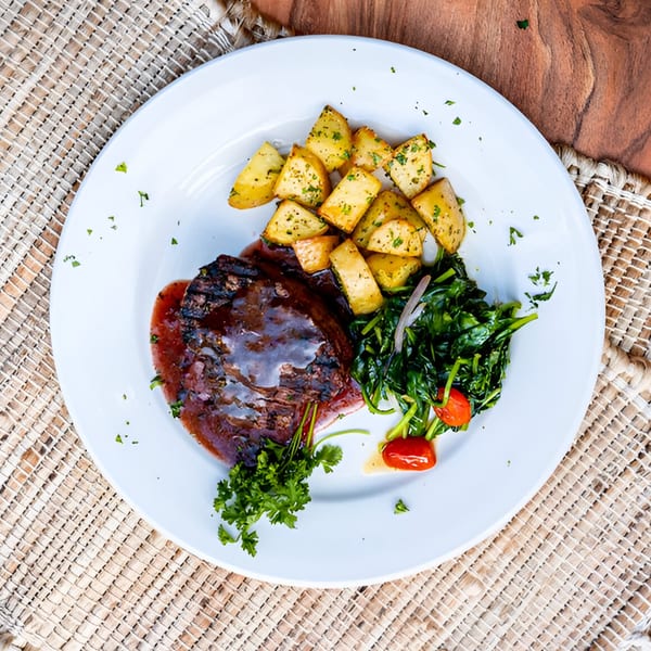 La Bella Luna's steak with sauce, roasted potatoes, spinach, and cherry tomatoes on a white plate.