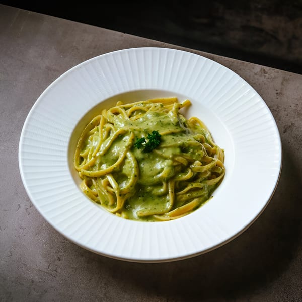La Bella Luna's linguine pasta with creamy green pesto sauce, garnished with parsley in a white bowl.