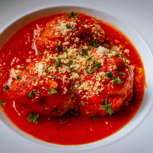 Three Italian meatballs in rich red marinara sauce, topped with grated cheese and fresh parsley.